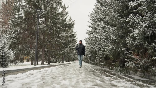 Snowy avenue caucasian traveler walking, scanning treeline while adjusting backpack strap, beanie and insulated coat, closeup gaze and breath in cold air, exploratory urban nature blend