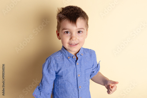Boy of three years in a blue shirt on a yellow background. Emotional portrait.