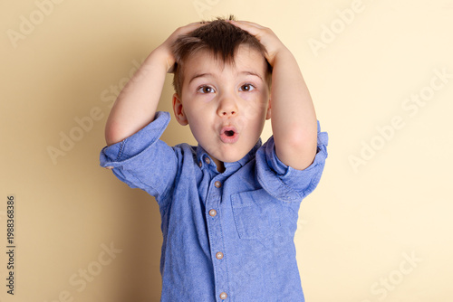Boy of three years in a blue shirt on a yellow background. Emotional portrait.