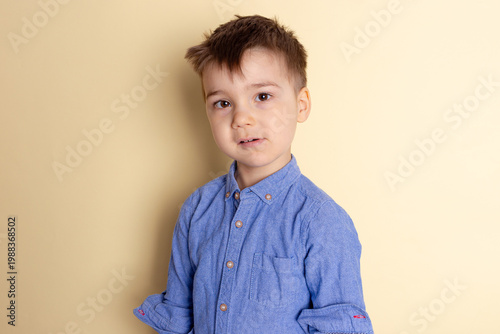 Boy of three years in a blue shirt on a yellow background. Emotional portrait.
