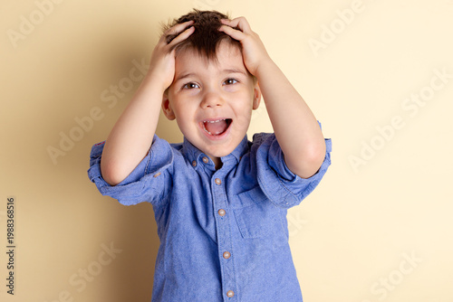 Boy of three years in a blue shirt on a yellow background. Emotional portrait.