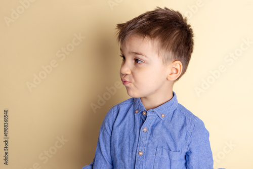 Boy of three years in a blue shirt on a yellow background. Emotional portrait.