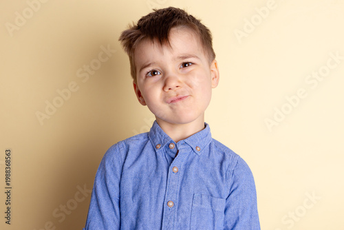 Boy of three years in a blue shirt on a yellow background. Emotional portrait.