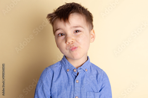 Boy of three years in a blue shirt on a yellow background. Emotional portrait.