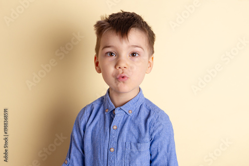 Boy of three years in a blue shirt on a yellow background. Emotional portrait.