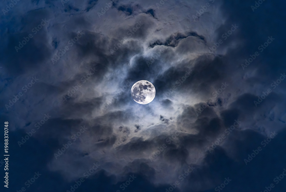 Fototapeta premium A full moon shines through a dramatic, cloudy night sky.