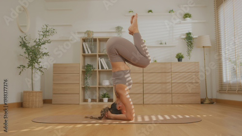 Εκτύπωση καμβά Asian yoga woman doing headstand in bright home studio with calm pose and soft l