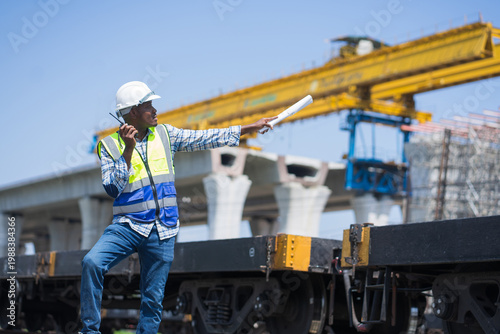 A civil engineer using a walkie-talkie and pointing at a large construction site