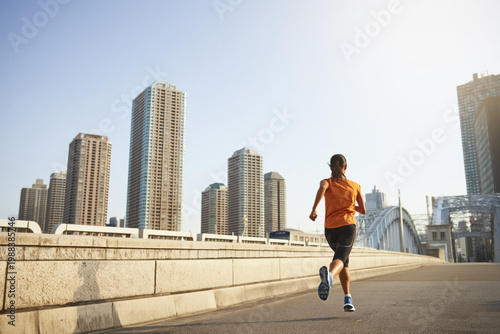 Asian female runner, running across a bridge in Japan, with high-rise buildings in the background