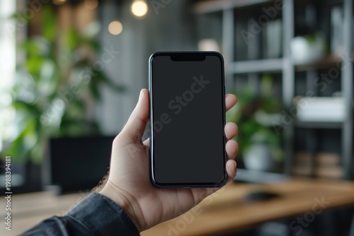 Hand Holding Smartphone with Black Screen in Modern Office Setting
