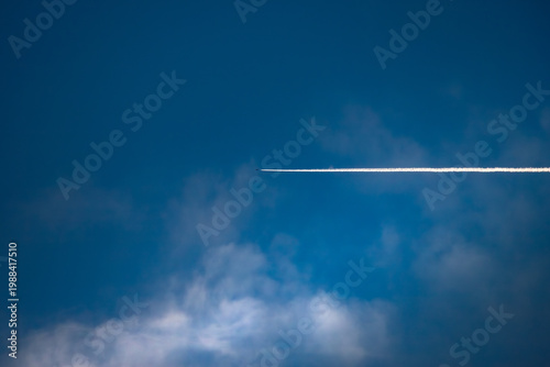 Airplane contrail in a deep blue sky with soft white clouds