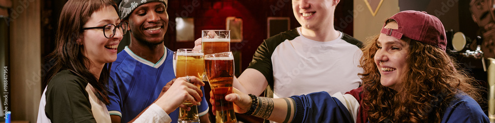 Fototapeta premium Multiethnic young adults clinking beer glasses in bar, celebrating friendship and social gathering. Ideal for nightlife marketing, youth lifestyle campaigns, community promotion