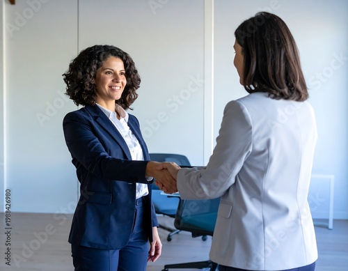 Two businesswomen shaking hands in office.