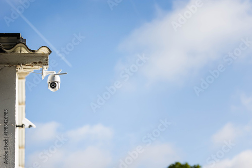 Une caméra de sécurité vidéo accrochée sur un bâtiment, on voit en grande partie le ciel en fond