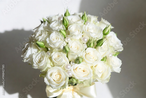 A white rose bouquet with pearls rests on a textured surface, illuminated by sunlight.