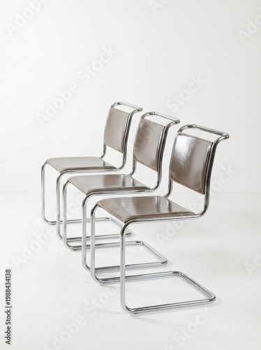 Three modernist chrome frame chairs with brown leather seats and backs, arranged in a row against a white background.