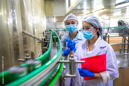 Fotografie Women food safety inspectors in hairnets and gowns inspecting canning process at
