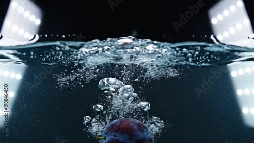Dramatic slow motion shot of a plum plunging into water creating a splash with background lights