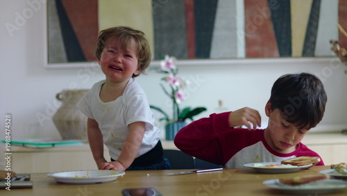 Photography Young children sitting at table during mealtime with one child crying and pointi