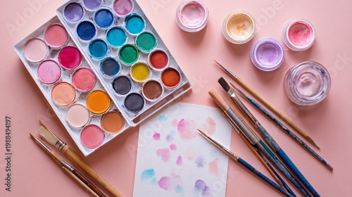 Pastel spring flat lay featuring watercolor paint palette, brushes, and paper on a soft peach background, gentle natural lighting, artistic arrangement with subtle paint stains and airy composition