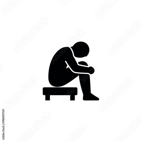 Silhouette of a person sitting alone on a stool head down conveying sadness or contemplation.