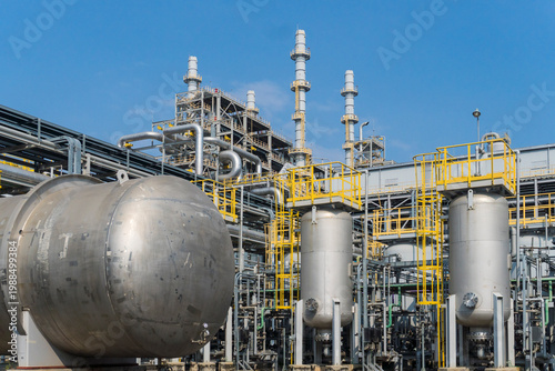 Fotografie Industrial facility with large metallic tanks and pipes under clear blue sky
