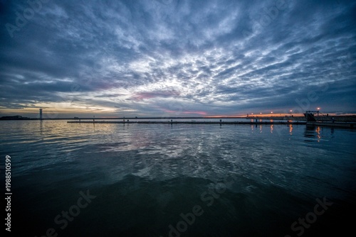 Foto Calm seascape at dusk with dramatic clouds and distant pier lights reflected in still water at Viareggio, Italy