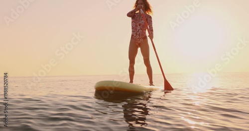 A happy young woman walking on a sup board by the sea during her summer vacation. Slow motion