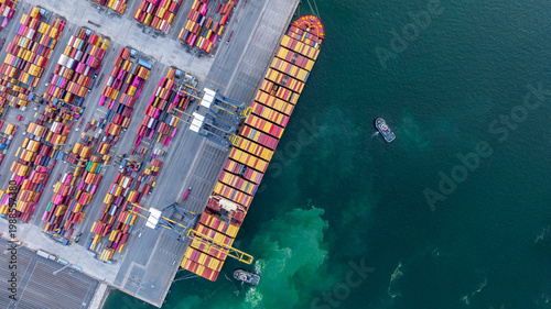 Aerial view container cargo ship at deep sea port terminal with tugboat assisting container cargo ship, Global trade and maritime supply chain, Logistics and transportation freight business industry.