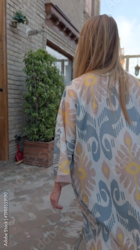 Back view woman in Uzbek robe walking old street in Tashkent city