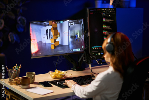 Принти на полотні Young adult woman streaming gameplay on computer, wearing headset and speaking into microphone while monitoring live chat