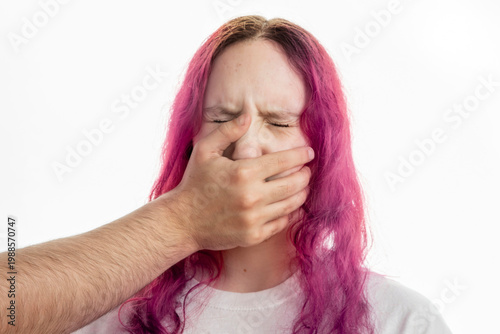Close up of a young woman with dyed pink hair being silenced by a male hand covering her mouth. Concept of domestic violence, coercive control, intimidation, abuse and fear.