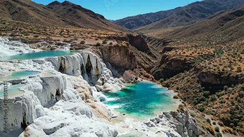 Aerial view of turquoise hot springs cascading over white rock formations in a desert canyon landscape on a sunny day