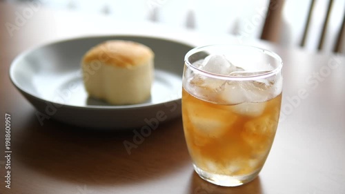 Vertical close-up of iced peach tea in a glass with fluffy Japanese sponge cake on wooden table for cafe, refreshment, and morning lifestyle concept