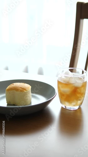 Vertical close-up of iced peach tea in a glass with fluffy Japanese sponge cake on wooden table for cafe, refreshment, and morning lifestyle concept