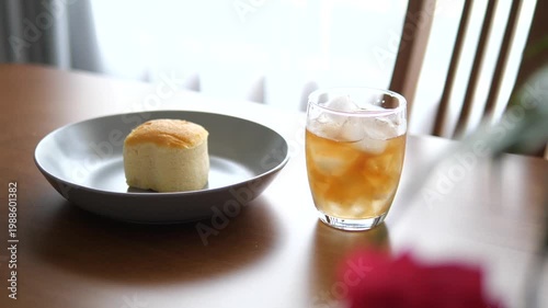 Vertical close-up of iced peach tea in a glass with fluffy Japanese sponge cake on wooden table for cafe, refreshment, and morning lifestyle concept