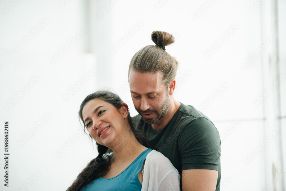 Fototapeta premium Father's Day Concept, affectionate couple embracing indoors with smiling woman and man in casual clothing near bright window