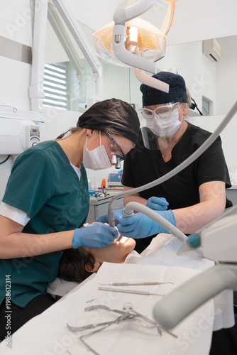 Medical specialists performing dental surgery and tooth treatment in stomatology clinic. Professional dentist and nurse using drill and saliva ejector for patient oral care process.
