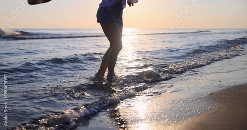 Happy woman is walking on the sandy beach in a red dress against sunrise. Slow motion