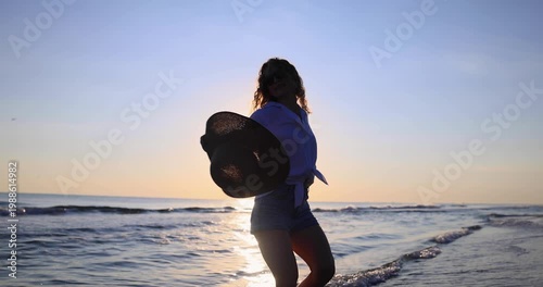 Happy woman is walking on the sandy beach in a red dress against sunrise. Slow motion