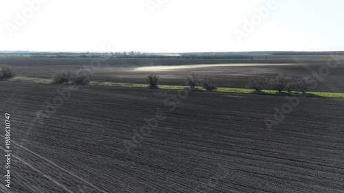 Drone shot over vast agricultural land showing wind erosion and dust patterns on dry soil. Wide panoramic view of cultivated black earth with light sandy sections. Process of soil degradation.