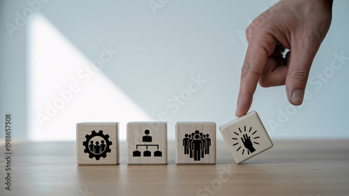 A hand placing a wooden block with a hand icon into a row of blocks with business and teamwork symbols.