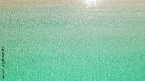 Shallow turquoise sea water lapping onto white pebble shore of secluded beach