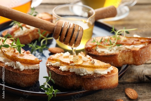Bild auf Leinwand Dripping honey onto delicious bruschettas with cream cheese, pears, almonds and