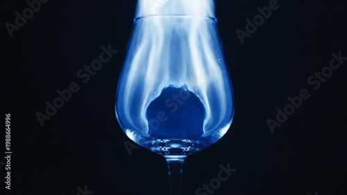 Blue fire burning inside a clear glass against black background