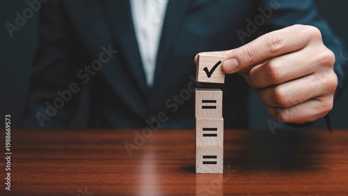 A businessman placing a checkmark on a wooden block above three equal signs on a desk
