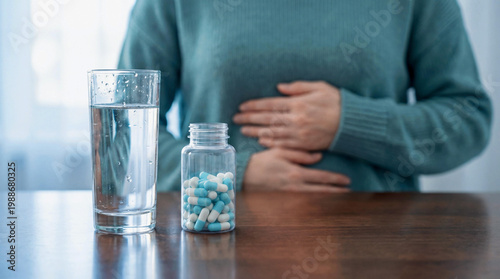 Person experiencing stomach pain, clutching abdomen. Medication bottle and water for upset stomach and abdominal pain relief
