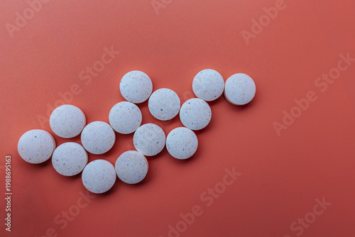 Obraz na płótnie White speckled tablets arranged in an arrow shape against a coral background, captured in a clean, minimalist composition