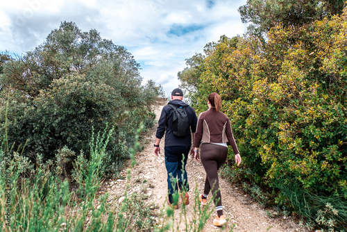 Fotografie Couple hiking uphill on a narrow green trail, back view, enjoying an active outd