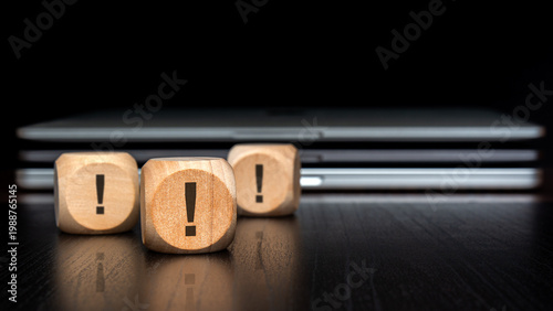 Multiple exclamation marks on wooden blocks. Blurred laptops and dark background. Cybersecurity and IT risk concept.
